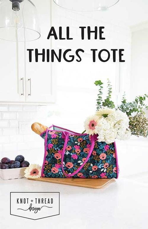 May include: A floral tote bag with pink handles and a dark blue background. The bag is filled with a baguette and a bouquet of white flowers. The text 'ALL THE THINGS TOTE' is displayed above the bag. The text 'KNOT + THREAD design' is displayed below the bag.